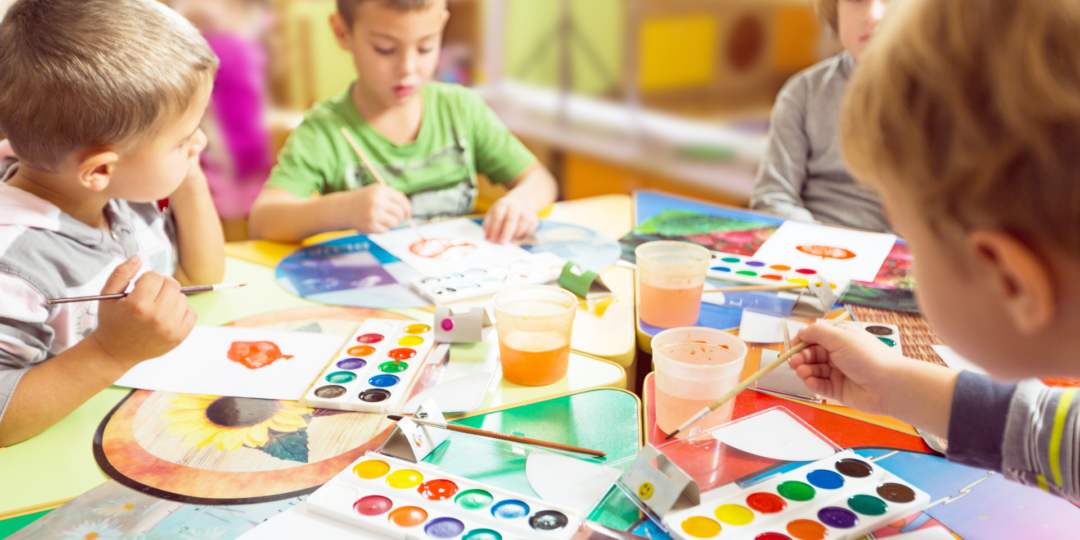 Groupe d’enfants s’amusant autour d’une table en dessinant avec des palettes de couleurs