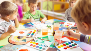 Groupe d’enfants s’amusant autour d’une table en dessinant avec des palettes de couleurs