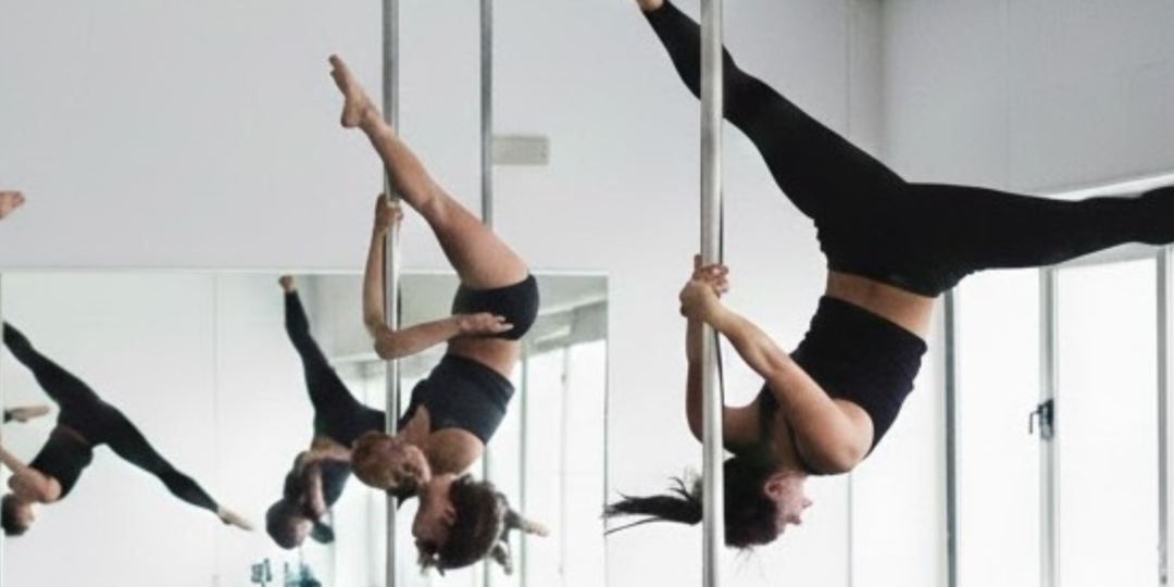 Cours de pole dance avec plusieurs femmes suspendues à la barre, jambes levées