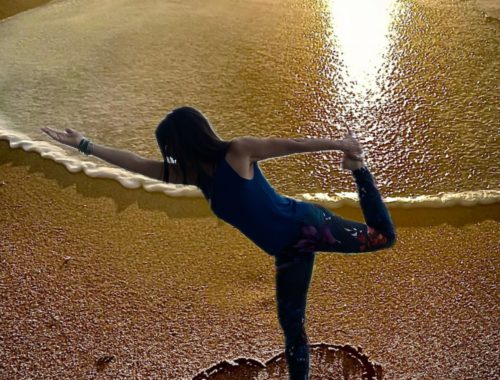Femme réalisant une posture de yoga sur une plage au coucher du soleil