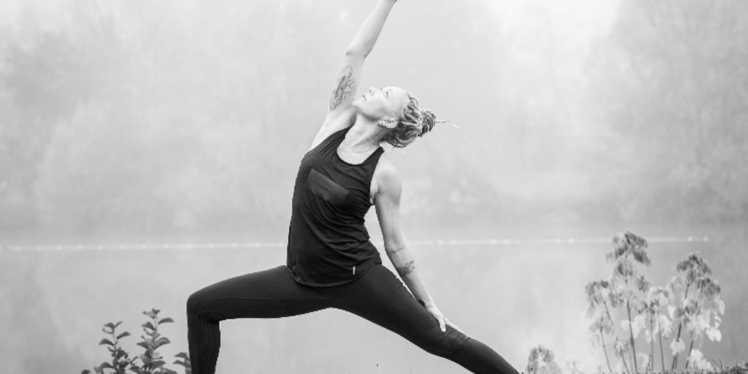 Photo noir et blanc représentant une personne près d'un lac pratiquant une posture de yoga.