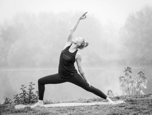 Photo noir et blanc représentant une personne près d'un lac pratiquant une posture de yoga.