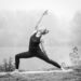 Photo noir et blanc représentant une personne près d'un lac pratiquant une posture de yoga.