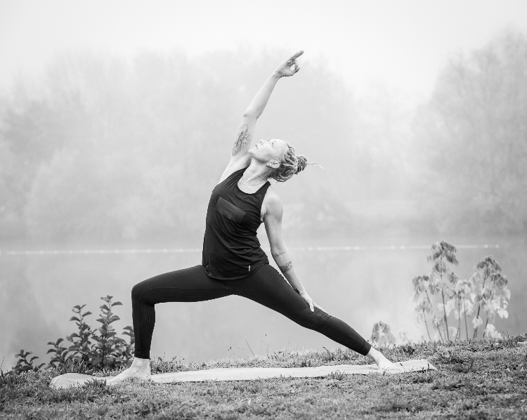 Photo noir et blanc représentant une personne près d'un lac pratiquant une posture de yoga.