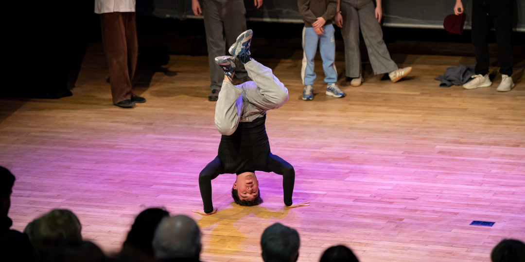 Spectacle où un jeune garçon effectue une figure de hip hop sur la tête.