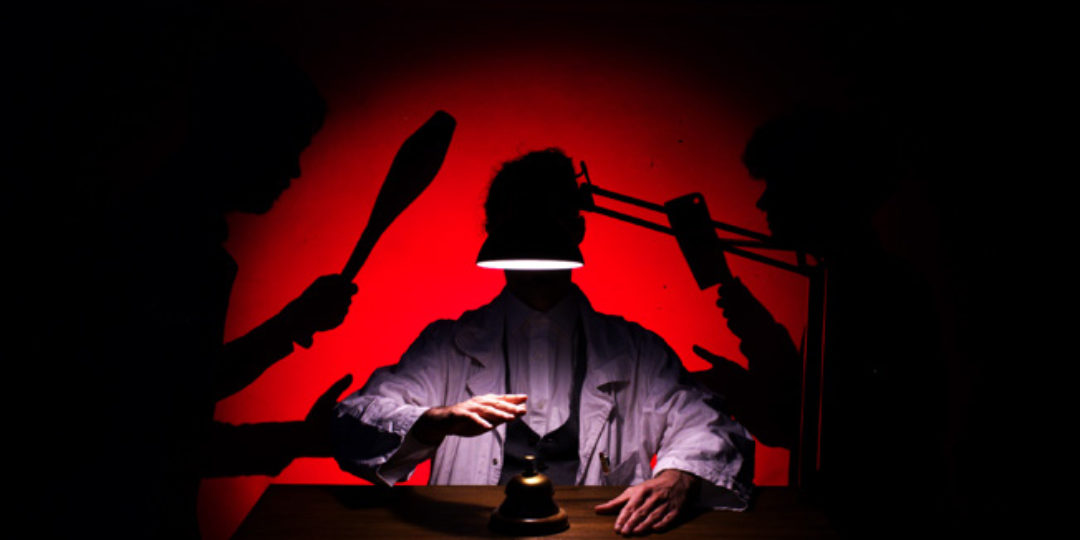 Scène de spectacle avec un personnage éclairé sous une lampe, dans une ambiance rouge et noire évoquant une quête de paix intérieure.