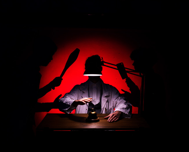 Scène de spectacle avec un personnage éclairé sous une lampe, dans une ambiance rouge et noire évoquant une quête de paix intérieure.