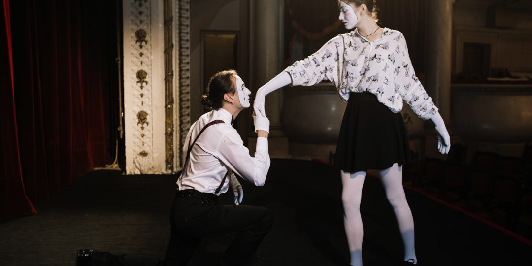 Deux artistes maquillés en mime interprètent une scène de théâtre burlesque sur une scène, illustrant un atelier d'expression corporelle et de jeu théâtral.
