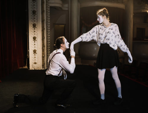 Deux artistes maquillés en mime interprètent une scène de théâtre burlesque sur une scène, illustrant un atelier d'expression corporelle et de jeu théâtral.