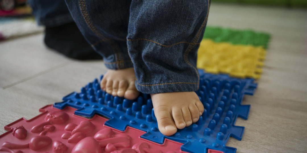 Jeune enfant marchant pieds nus sur un parcours sensoriel lors d'un atelier parent-bambin dédié au développement de la motricité.