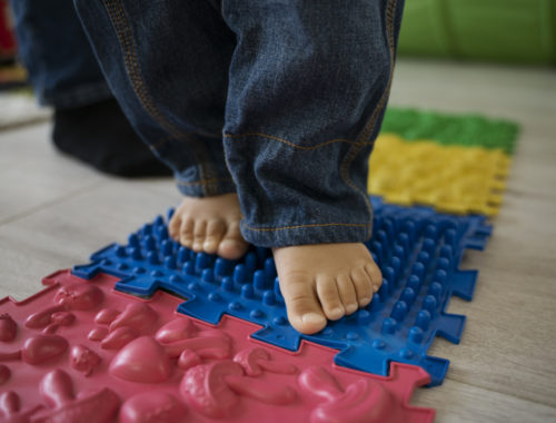 Jeune enfant marchant pieds nus sur un parcours sensoriel lors d'un atelier parent-bambin dédié au développement de la motricité.
