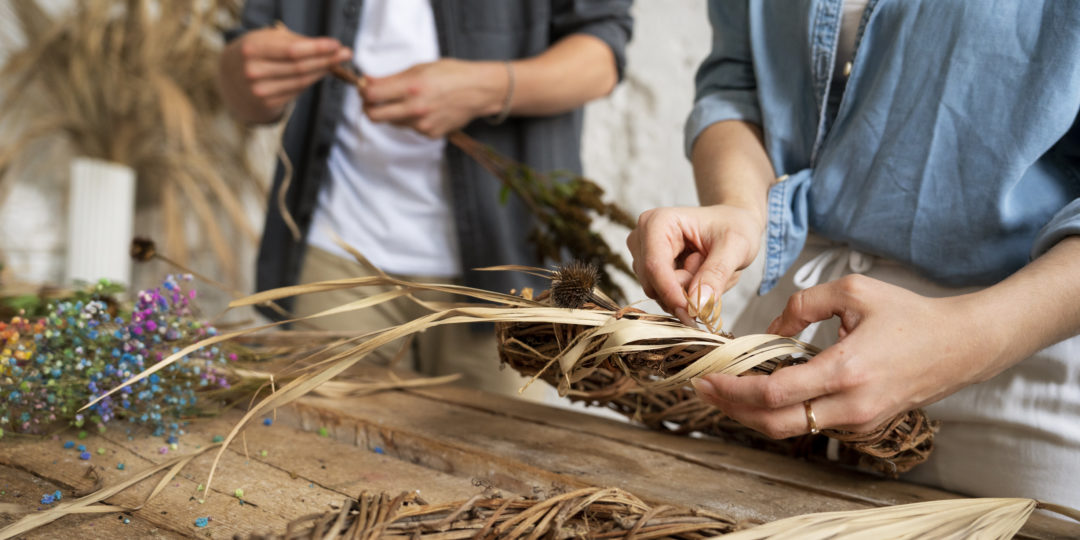 Participants réalisant un atelier de vannerie en tressant des fibres végétales pour créer un objet artisanal à la main.