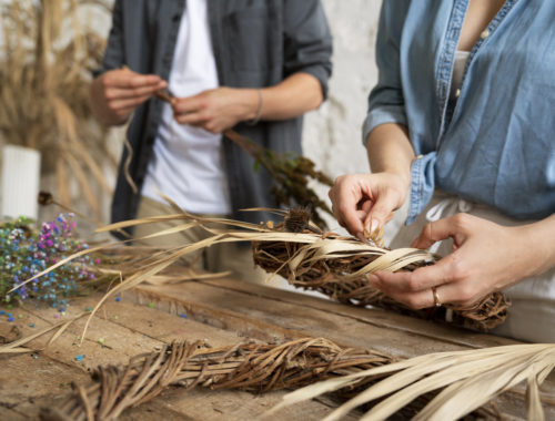 Participants réalisant un atelier de vannerie en tressant des fibres végétales pour créer un objet artisanal à la main.