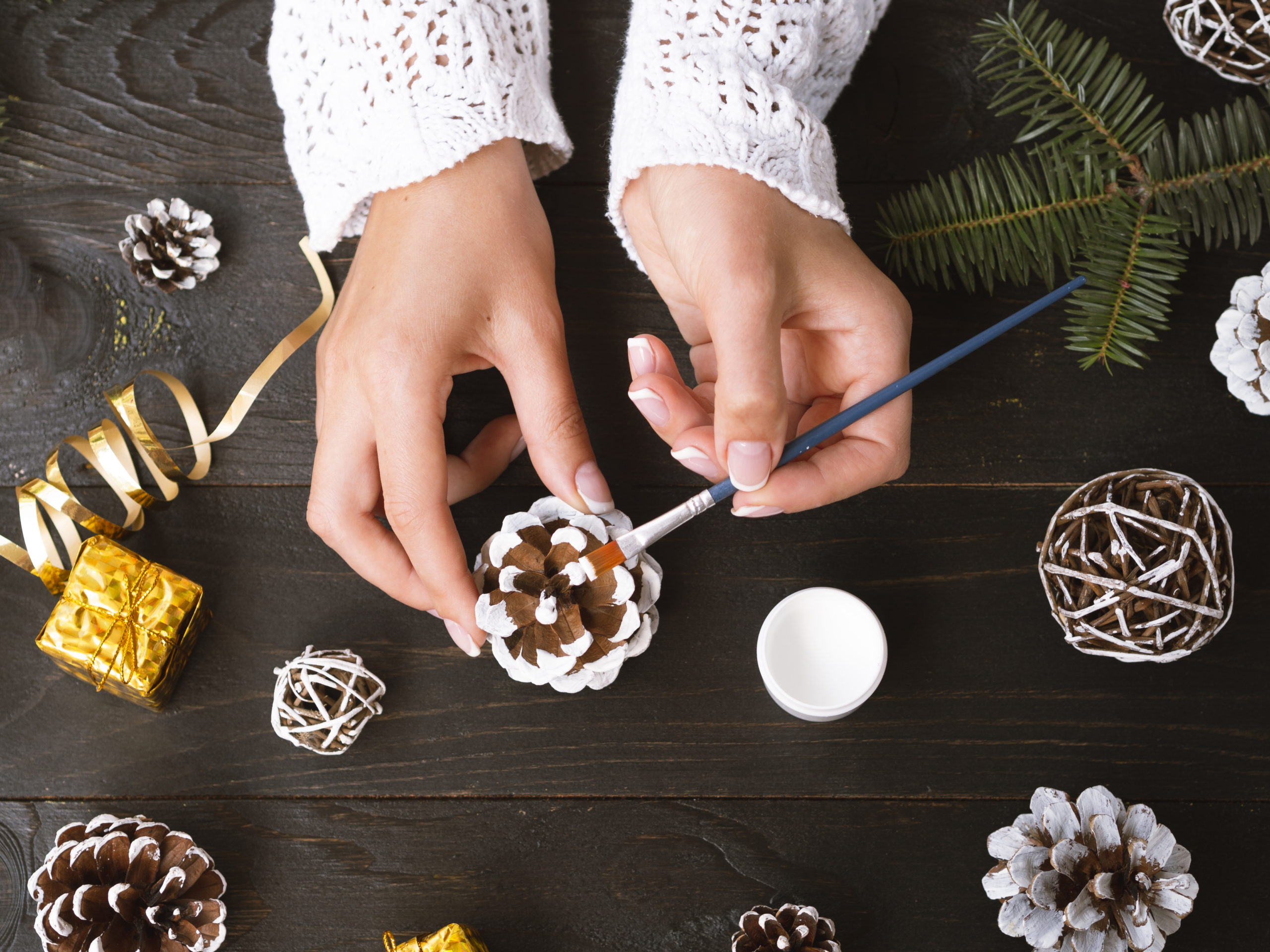 Personne décorant une pomme de pin lors d'un atelier créatif pour préparer les décorations du sapin de Noël.