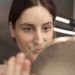 Conseillère en visagisme analysant les traits du visage d'une participante devant un miroir pour un conseil personnalisé.