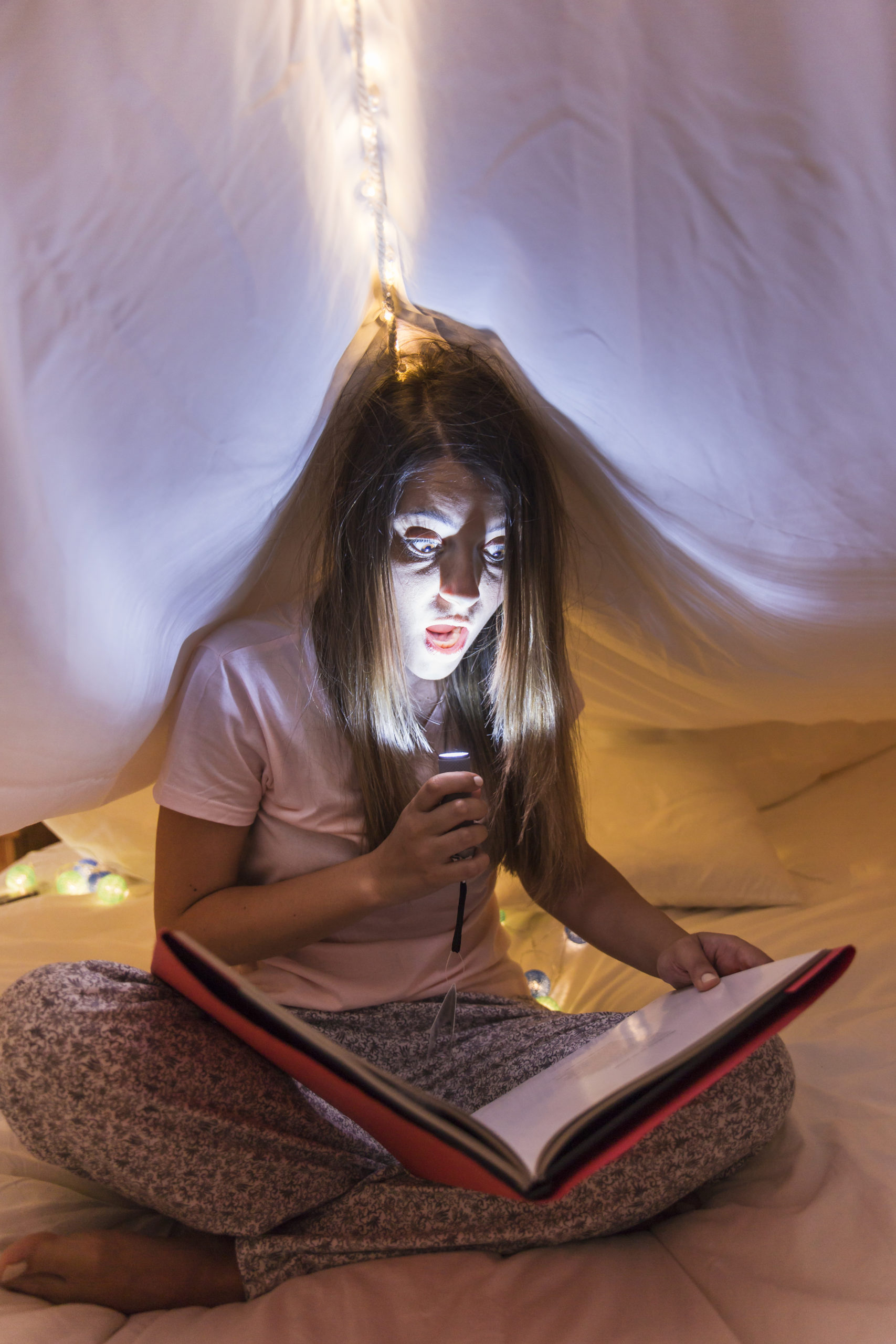 Personne lisant un livre à la lumière d'une lampe dans une ambiance chaleureuse, idéale pour un atelier de lecture ou un moment de conte.