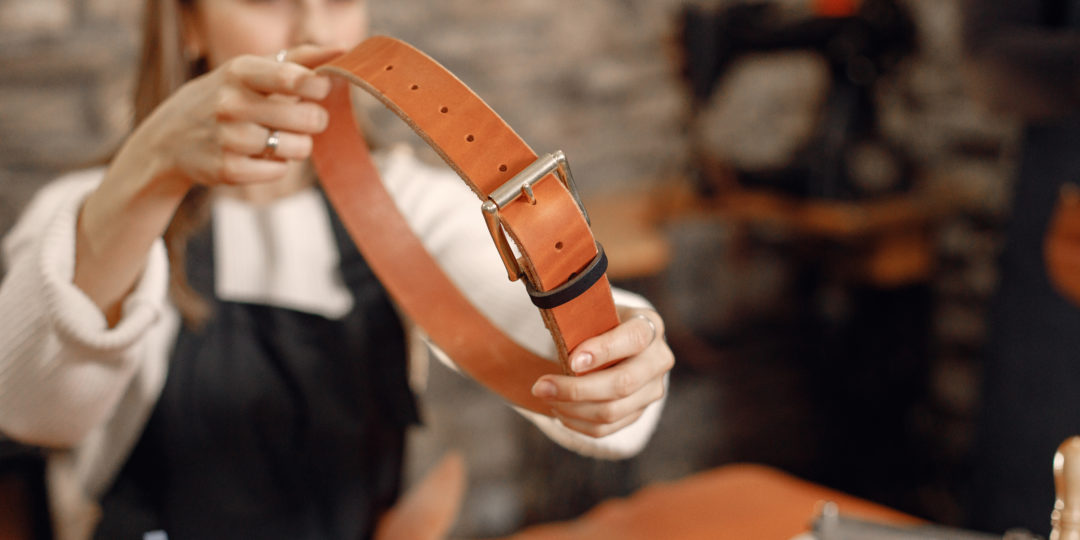 Personne tenant une ceinture en cuir fabriquée à la main dans un atelier de maroquinerie, illustrant un atelier de création artisanale en cuir.