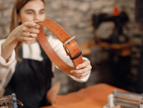 Personne tenant une ceinture en cuir fabriquée à la main dans un atelier de maroquinerie, illustrant un atelier de création artisanale en cuir.