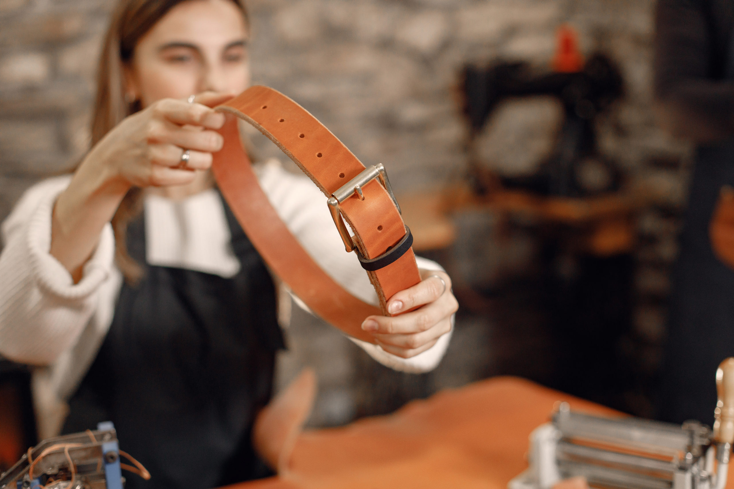 Personne tenant une ceinture en cuir fabriquée à la main dans un atelier de maroquinerie, illustrant un atelier de création artisanale en cuir.
